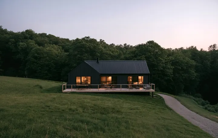 Dom z oświetlonymi oknami na skraju lasu o zmierzchu