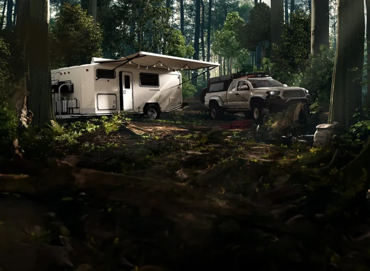 Camper with a trailer and pickup truck parked in a forest